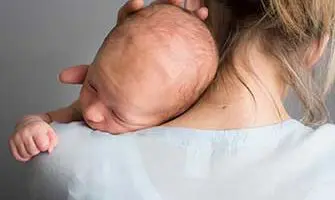Newborn baby peacefully resting on mother's shoulder, showcasing tender bond and affection between parent and child.