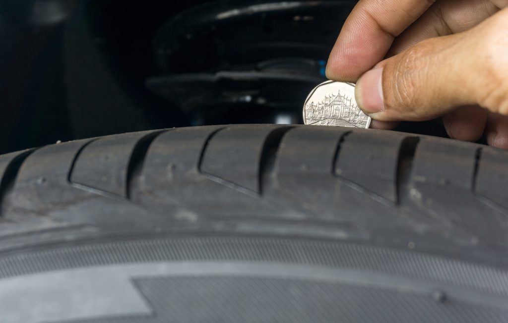 A person checks the tread depth of their tires using a quarter
