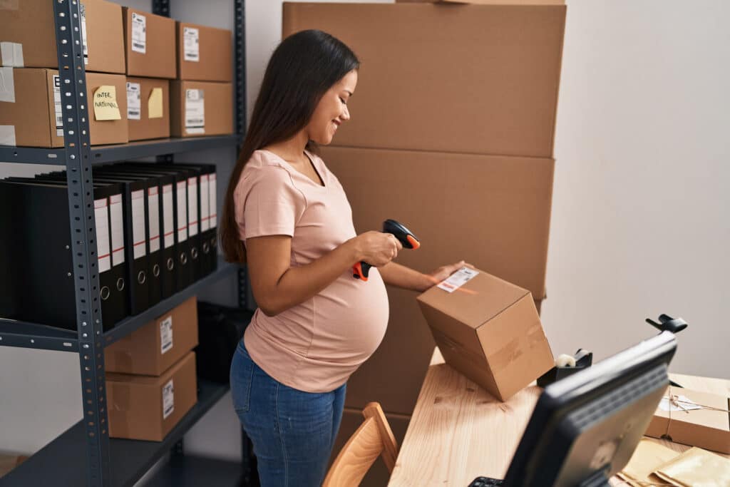 Young Latin Woman Pregnant Business Worker Scanning Package Label at Office Giroux Pappas Trial Attorneys